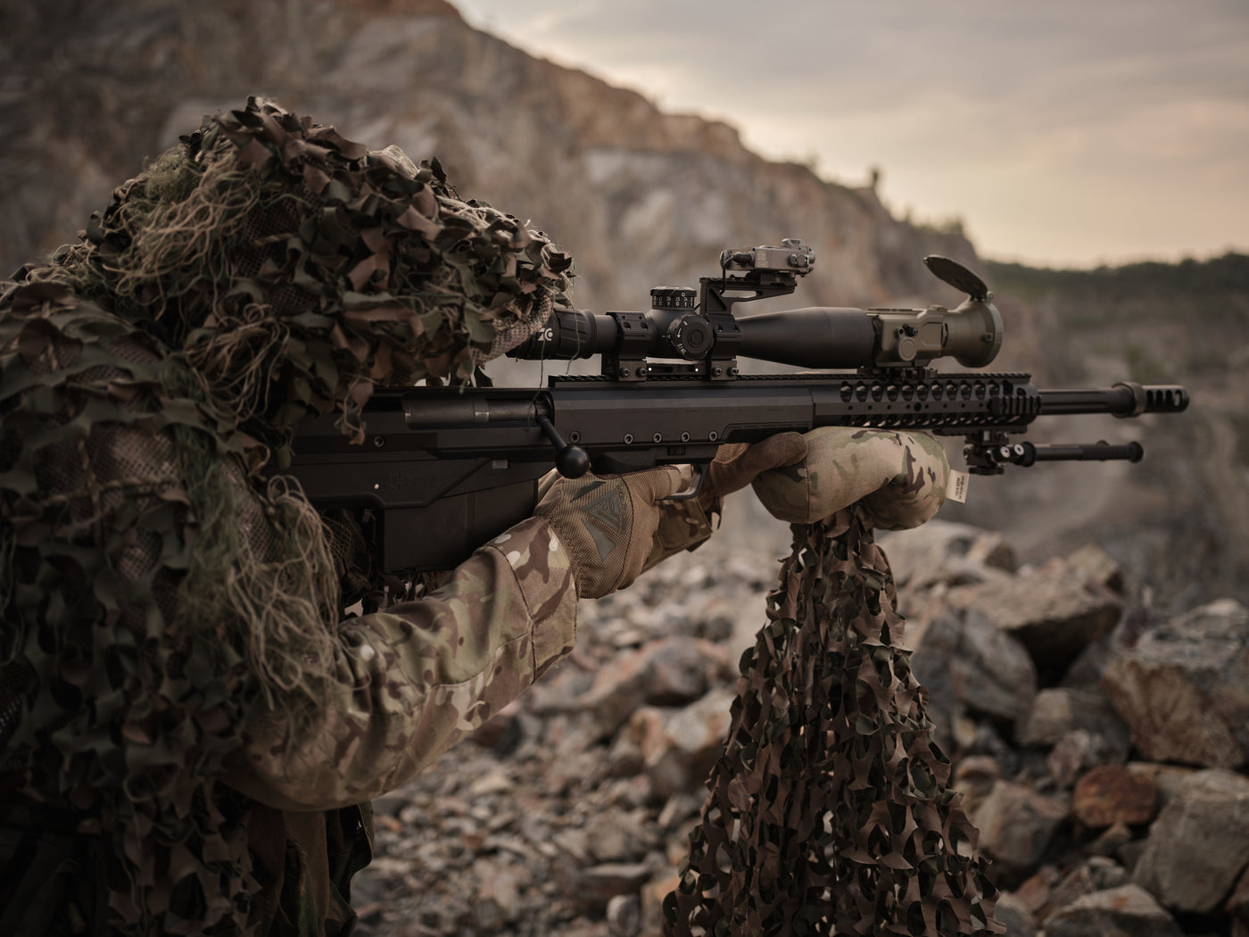 Ein Soldat im Tarnausrüstung zielt mit einem PumIR auf einem Scharfschützengewehr.